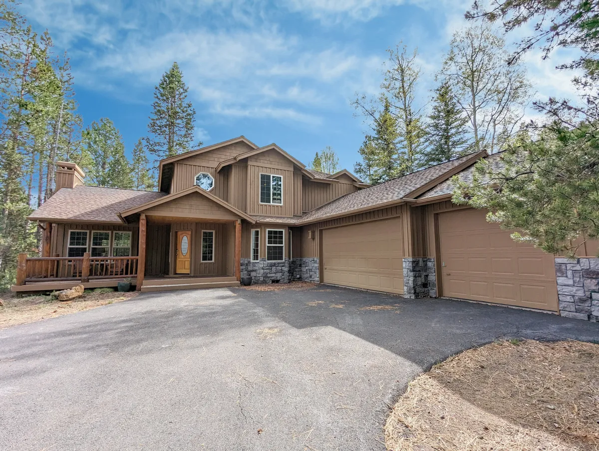 This image showcases the home's wooden front porch with inviting stone accents, large windows, and the surrounding pine trees, suggesting easy access to nature and outdoor activities. The porch area exudes tranquility and offers a visual connection to the natural setting of Sunriver.