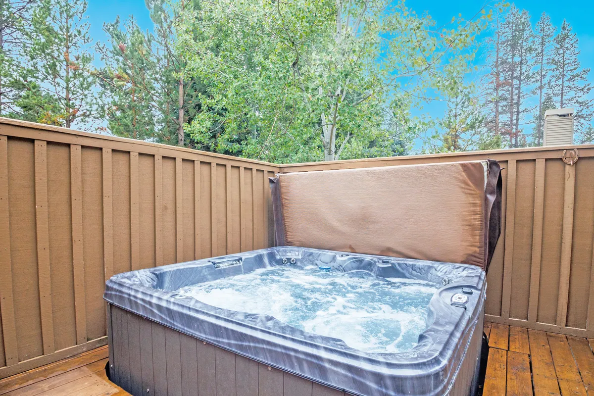 The shot displays a hot tub on a spacious wooden deck, surrounded by trees and natural landscaping. The scene captures the peacefulness of soaking in the tub while immersed in nature, embodying the essence of a relaxing resort experience.