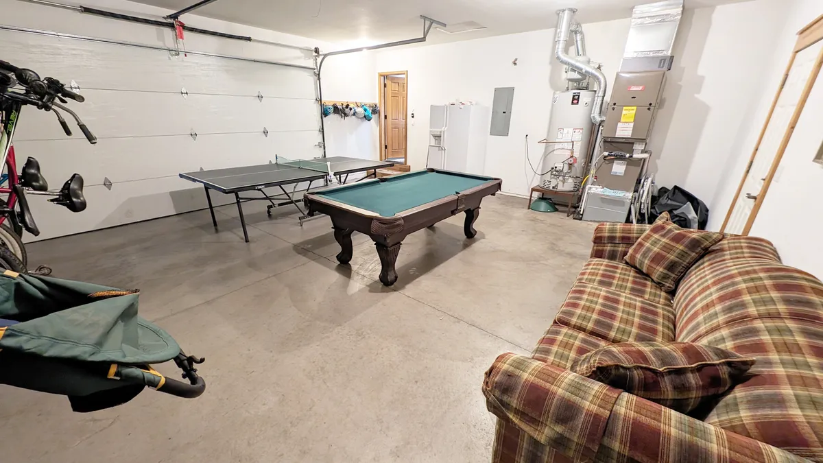 Inside a spacious garage recreation area, a pool table, ping pong table, and a cozy couch invite guests to enjoy friendly competition and relaxed fun. The bright space is perfect for group activities, game nights, and laughter after a day of adventure.