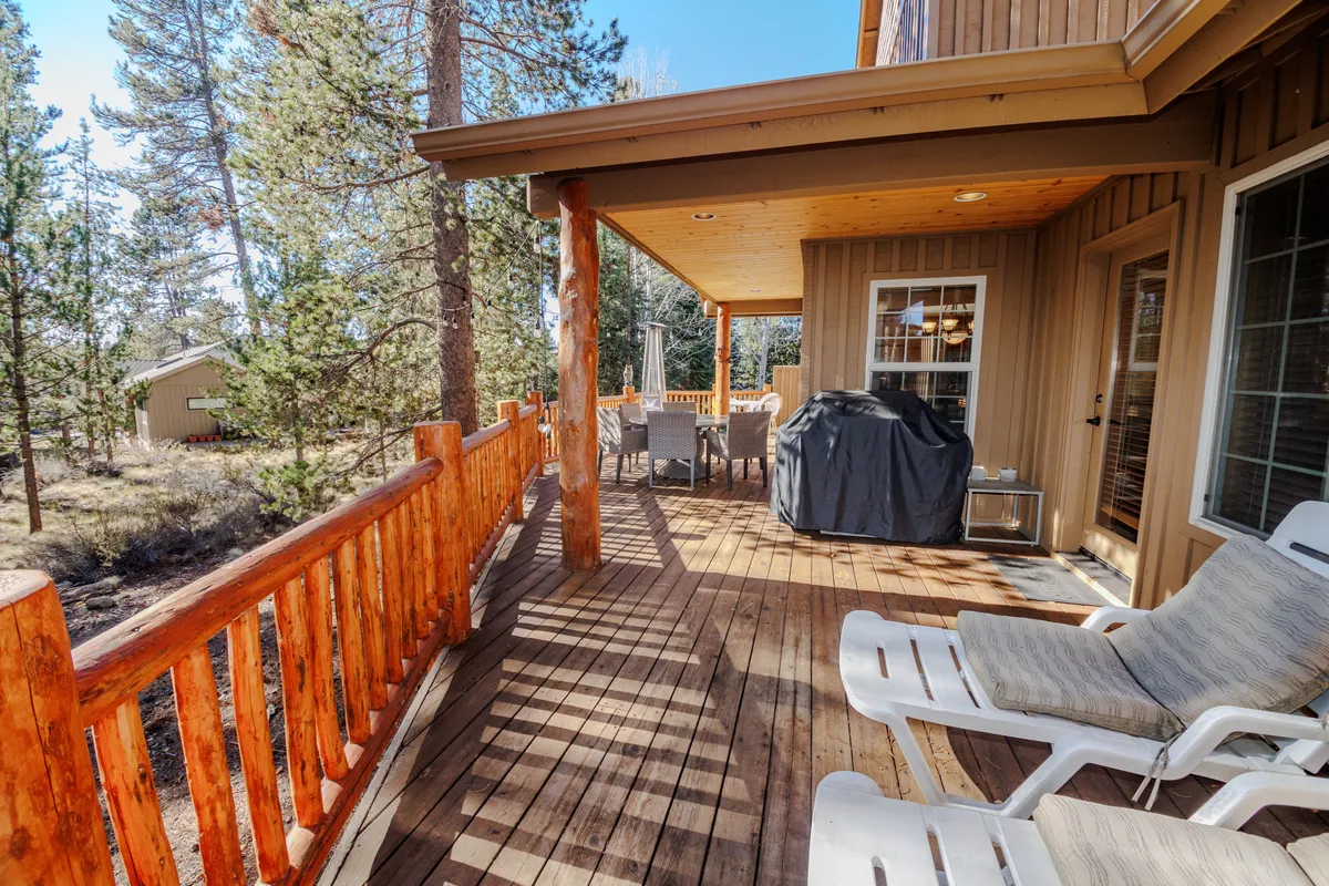 A welcoming back deck with wooden railing, outdoor seating, a grill, and surrounding trees, creating a perfect spot for enjoying mountain air and al fresco dining. The proximity to nature encourages guests to relax outdoors and extend their gatherings beyond the interior.