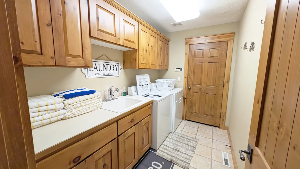 This image features a functional laundry room with a washer, dryer, folded towels, and wood cabinetry, emphasizing the practicality of prepping for and recovering from outdoor adventures.