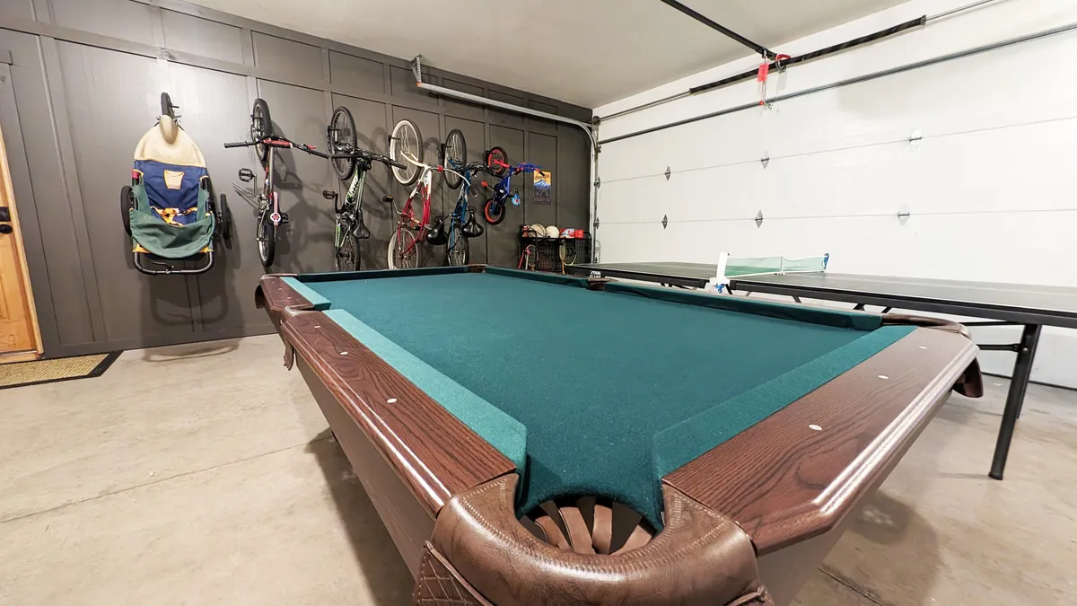 Inside the garage game zone, this image showcases a pool table, wall-mounted bicycles, and a folding table. The inviting recreation space is well-lit and designed for friendly competitions or prepping gear for a day outside.