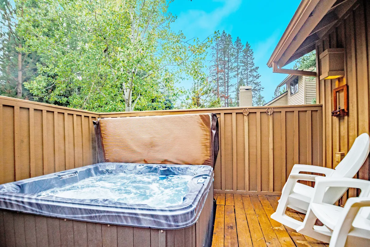 This exterior image features a private hot tub set on a wooden deck, surrounded by lush greenery and a white chair nearby. The tranquil ambiance invites relaxation and rejuvenation, highlighting direct access to the outdoors from the home.