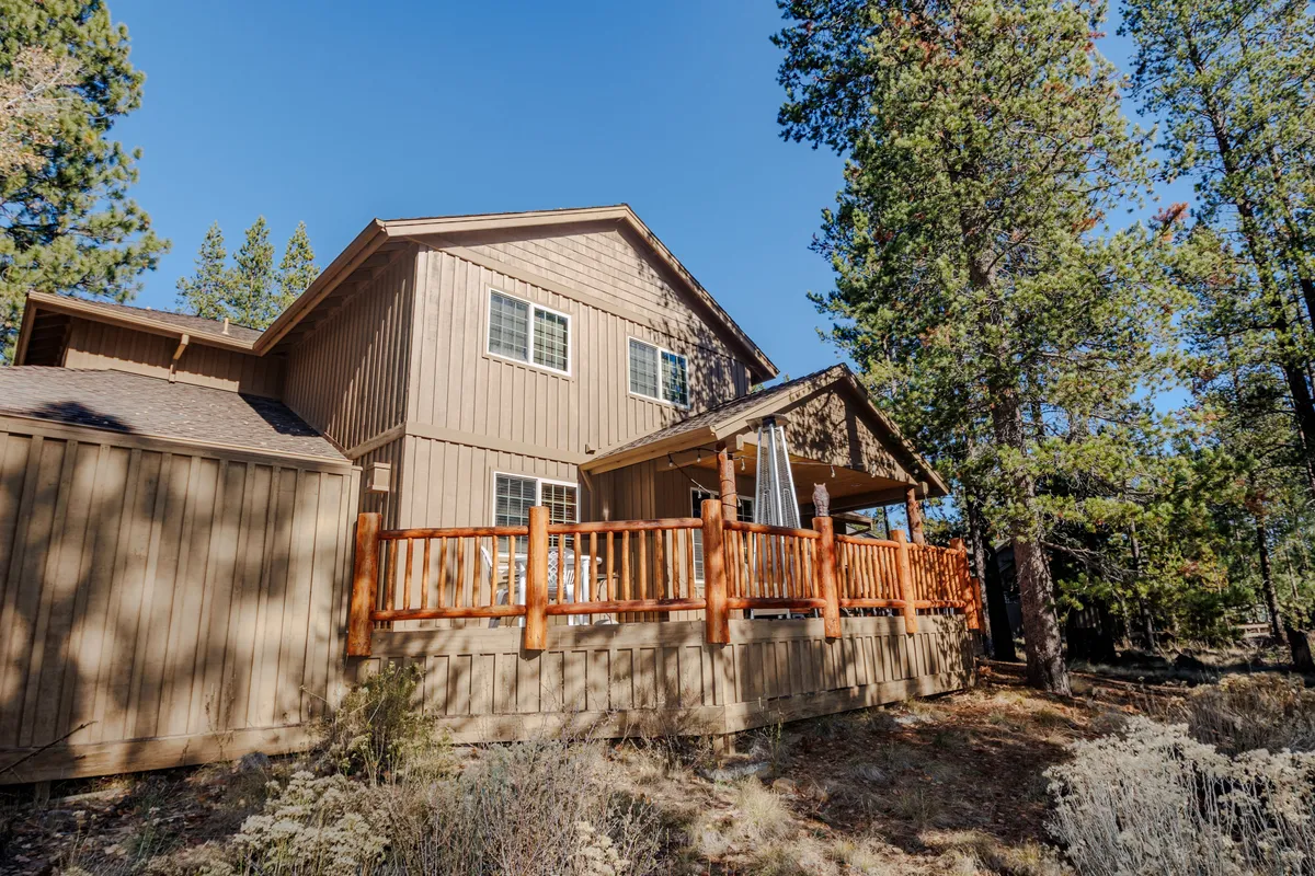 This image features a wooden deck surrounded by towering pine trees, with architectural details of the house visible in the background. The serene outdoor setting highlights the spacious deck area, perfect for gathering, relaxing, or preparing for outdoor adventures.